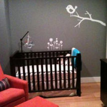Small modern neutral gray and orange baby nursery with white tree wall mural and orange glider