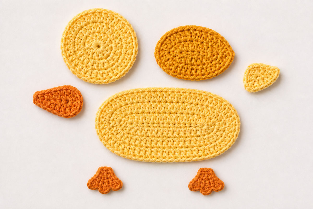 Partially assembled flat yellow crochet duck applique with the head, wing, orange beak and feet positioned on the body before final sewing