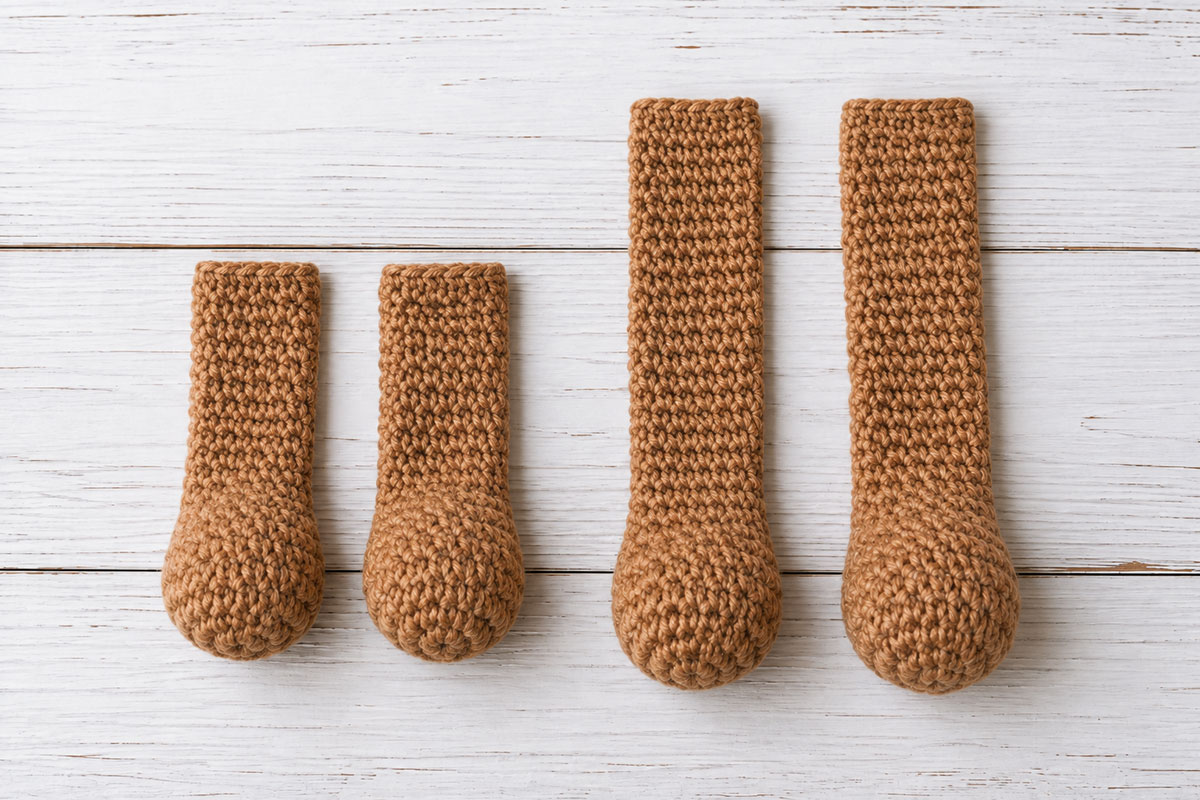 Two matching crochet bear snuggler arms and two longer legs with lightly stuffed rounded ends and flat unstuffed upper sections