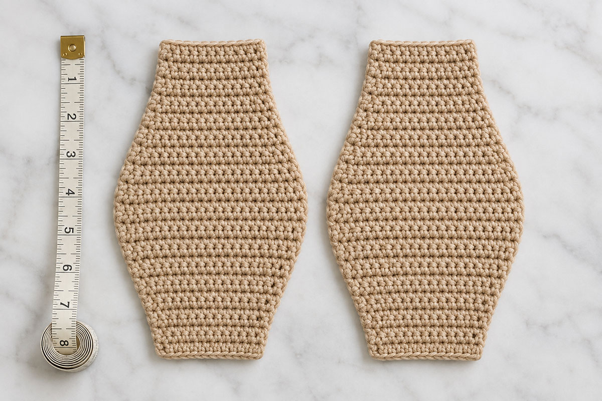 Two matching flat crochet bear snuggler body panels laid together beside a measuring tape before assembly