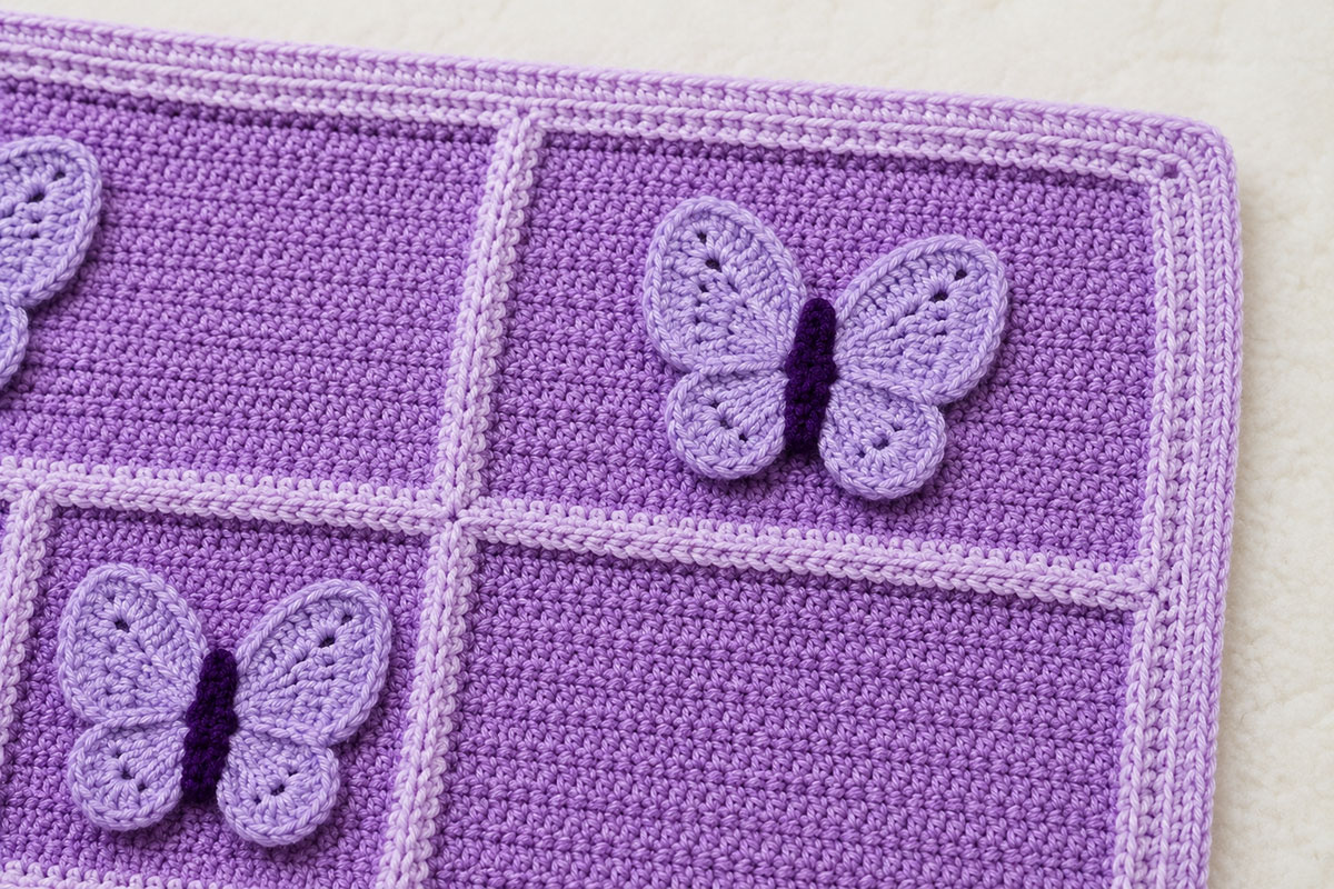 Close view of the light lavender five round crochet border surrounding framed squares and dimensional butterfly appliques on a baby blanket