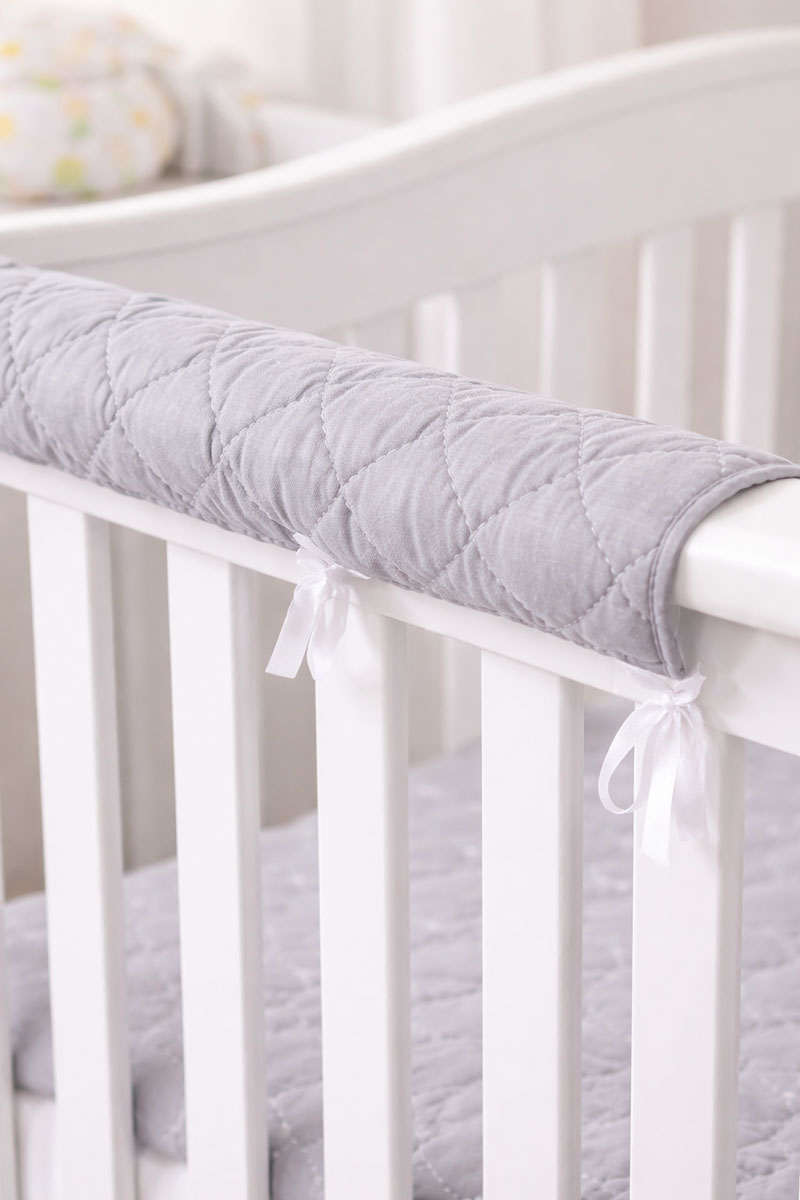 Close-up of a padded crib rail cover tied around the top rail