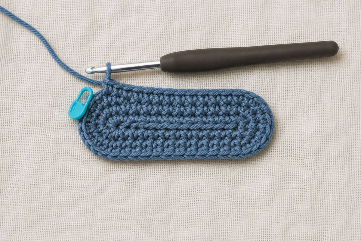 Oval crochet baby bootie sole showing rounded toe and heel increases with stitch markers
