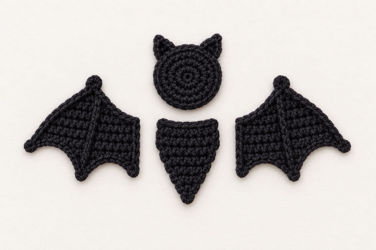 Crochet bat applique pieces with round head tapered body and two matching shaped wings laid out before assembly
