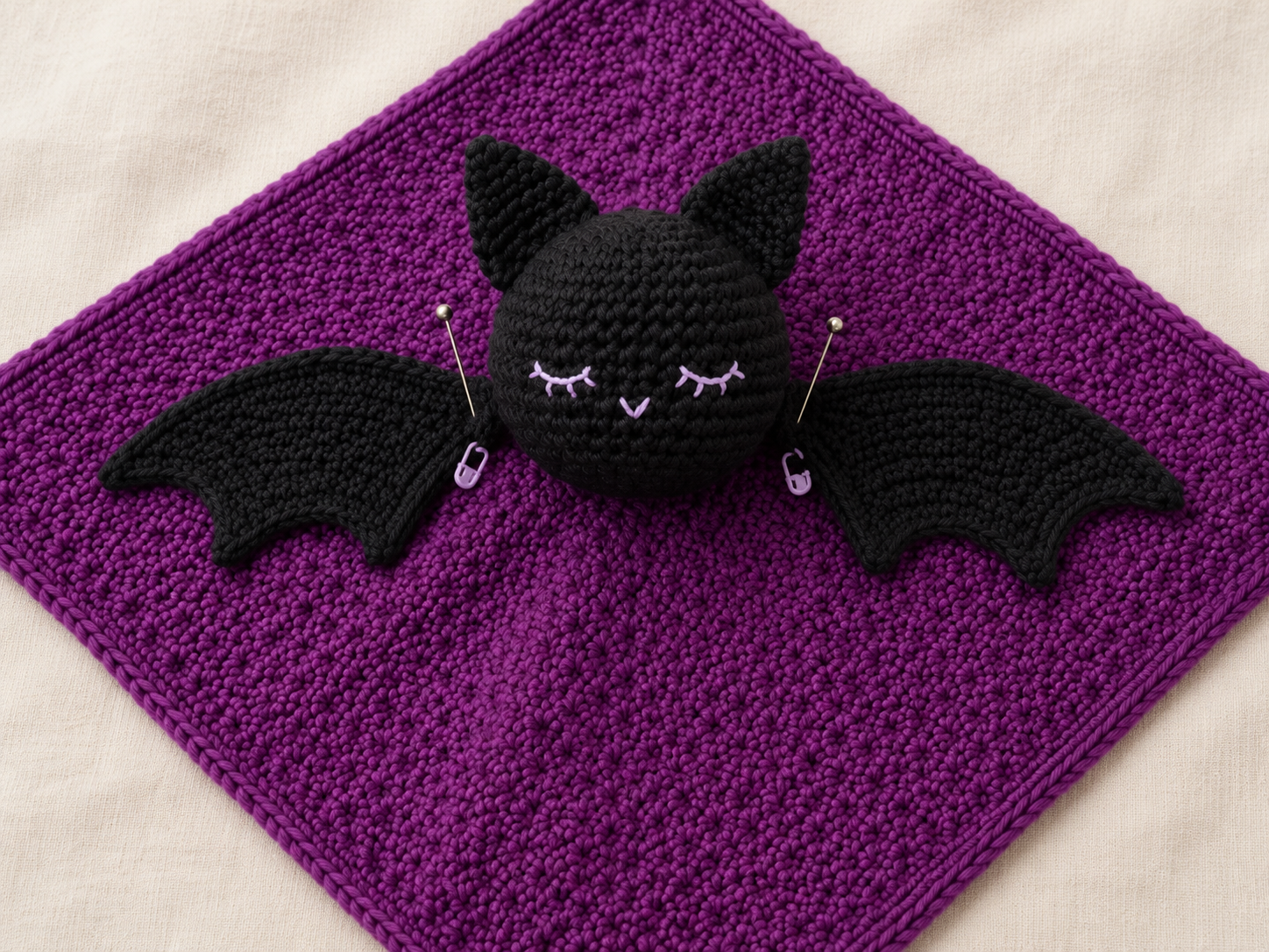 Close view of a crochet bat head and wings pinned to the center of a lovey blanket before final sewing