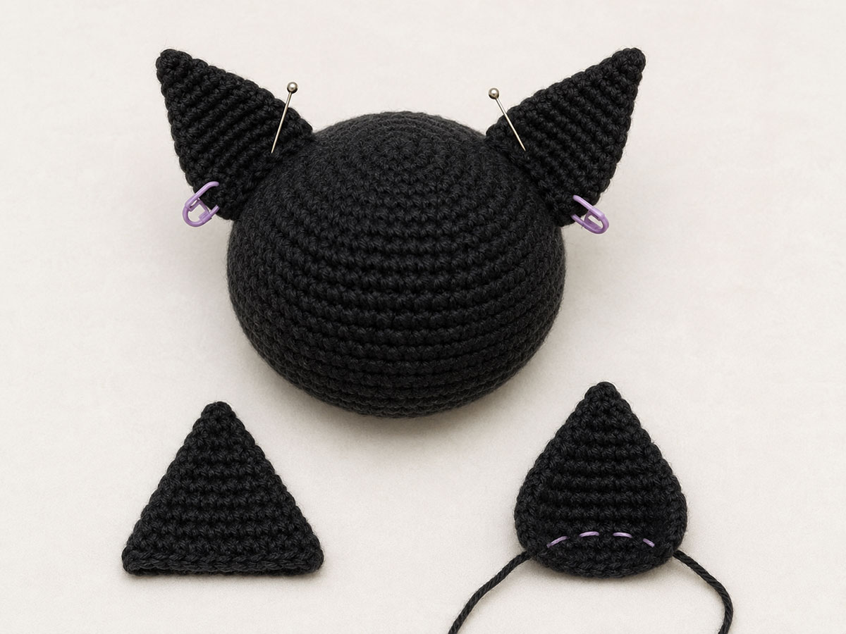 Two small pointed crochet bat ears pinned to the top of a bat lovey head before sewing