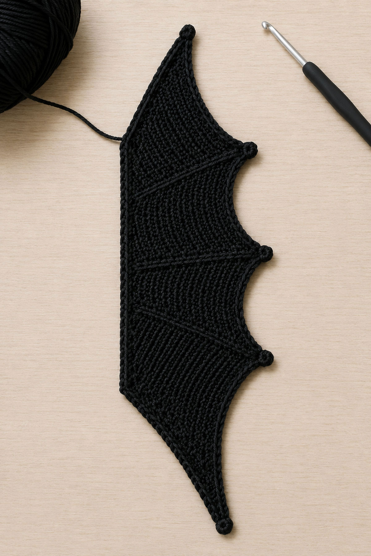 Crochet bat wing in progress showing the straight attachment edge widening body and shaped outer tip