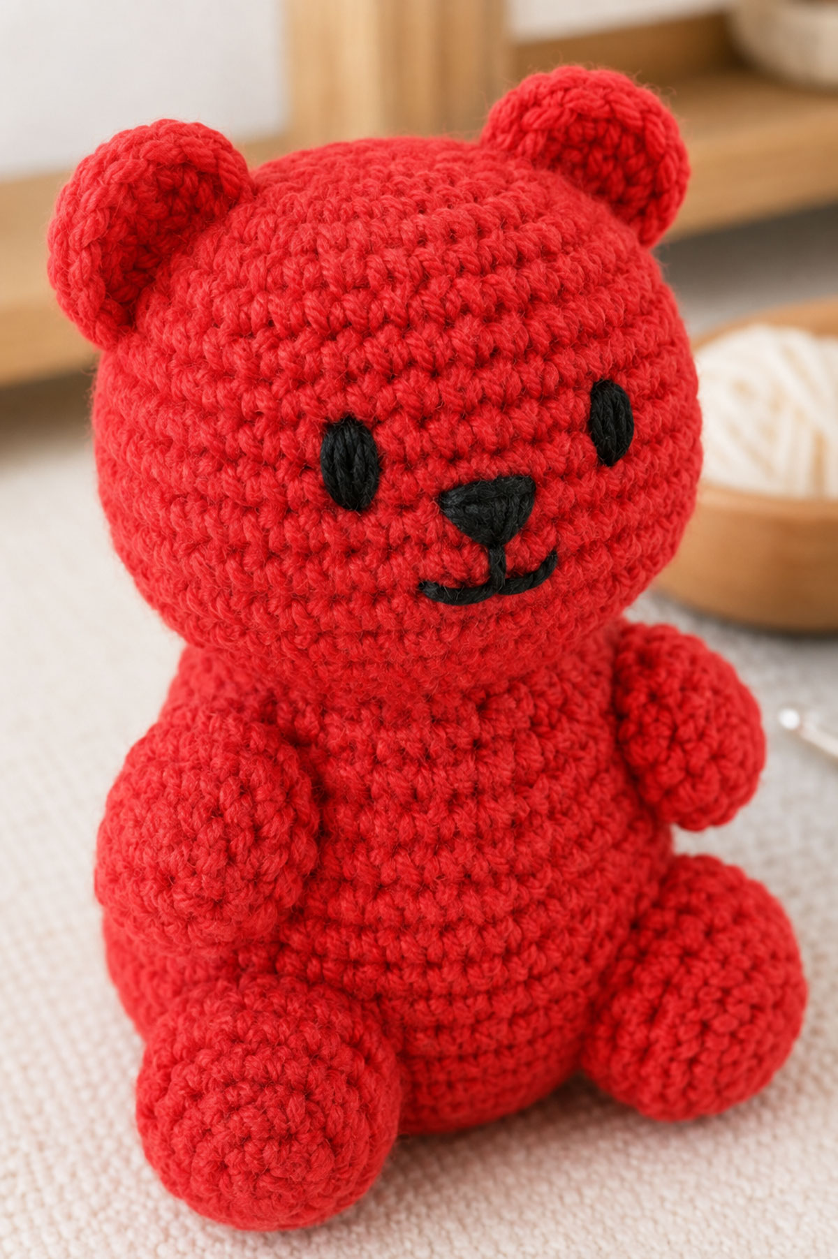 Close three-quarter view of a bright crochet gummy bear with small black satin stitch eyes compact embroidered nose and short stitched smile