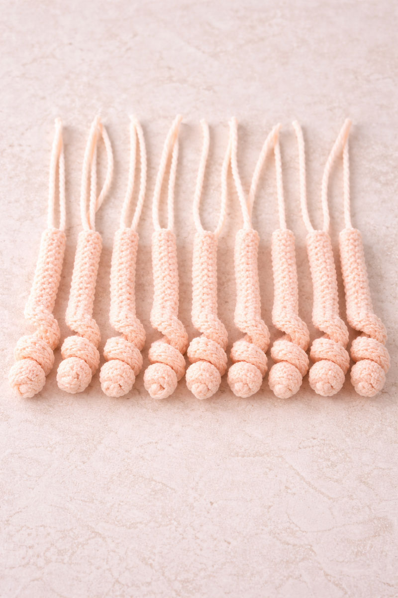 Ten crochet jellyfish tentacles with curled ends laid out before assembly
