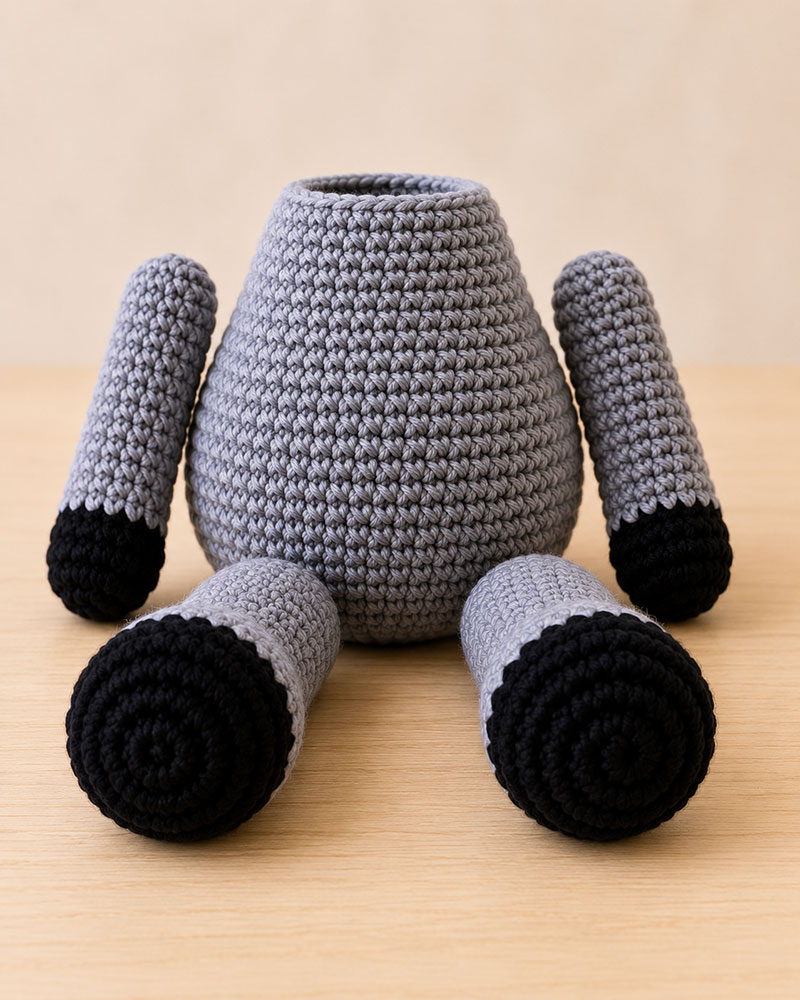 Crochet raccoon gray body black paws and oversized black feet before assembly