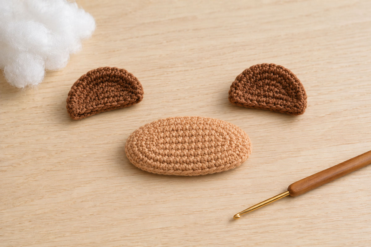Light tan crochet teddy bear muzzle beside two rounded brown crochet ears before assembly