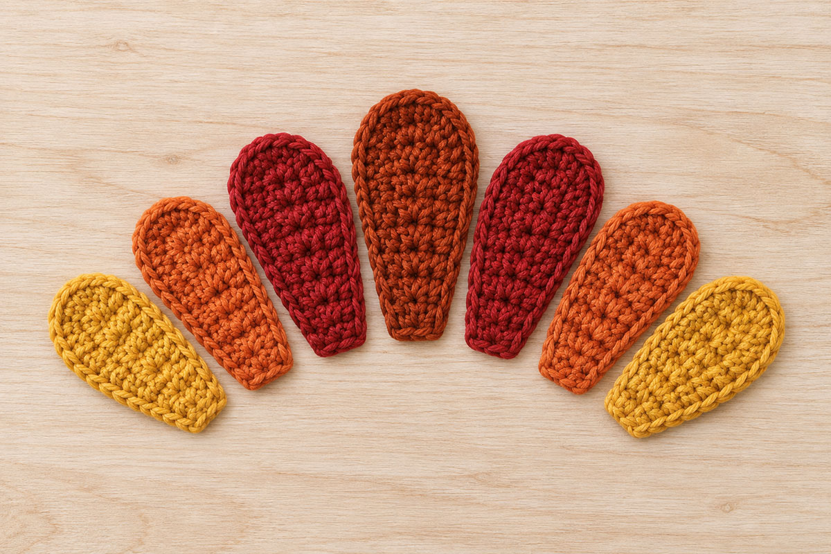 Seven separate crochet turkey tail feathers arranged from mustard to burnt orange, cranberry and deep rust with the center feather tallest