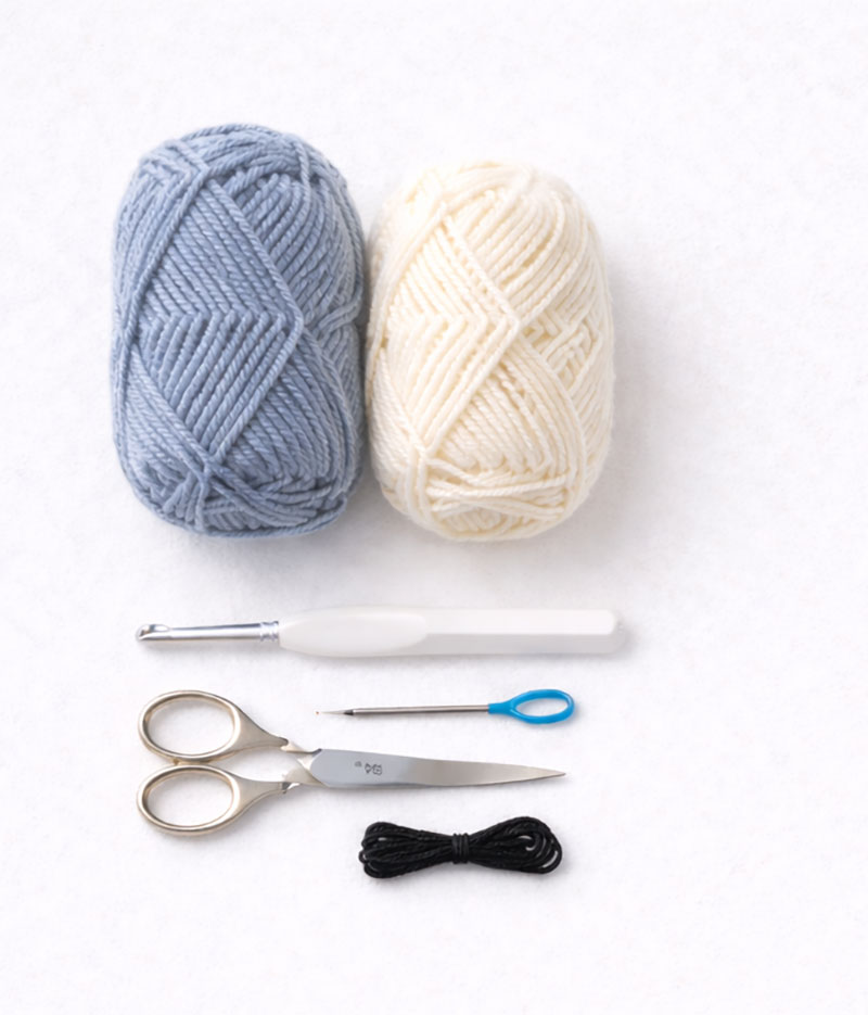 Yarn, crochet hook, scissors, and needle arranged for a crochet whale pattern