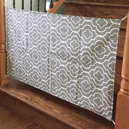 Homemade fabric baby gate made of heavy duty grey and white canvas with a modern geometric pattern.