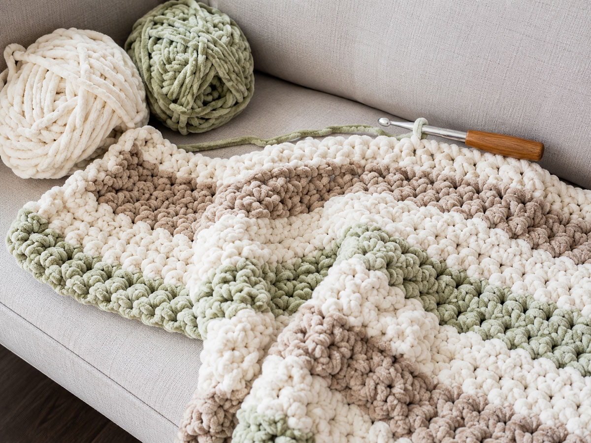 Partially completed ribbed chunky baby blanket folded across a project bag beside a large crochet hook