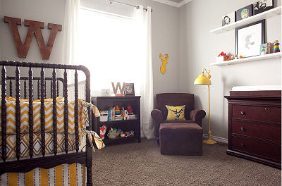 The sitting area in the forest themed nursery is lit by a modern yellow floor lamp and features a wooden, whitetail deer silhouette as a wall decoration.