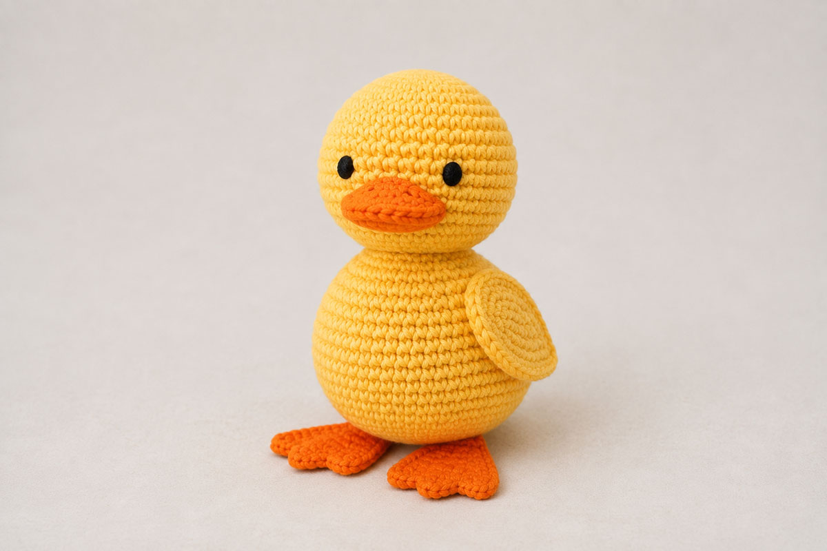 Finished yellow crochet duck with orange bill and webbed feet, flat wings and embroidered eyes