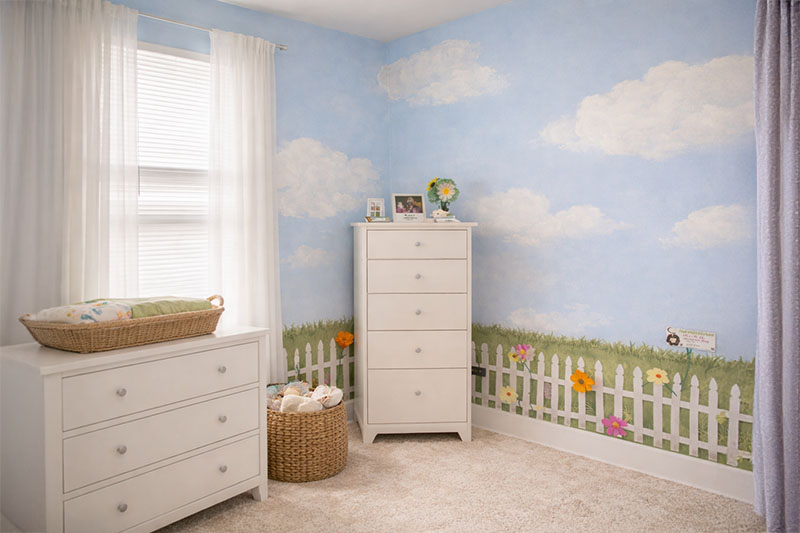 Hand-painted cloud mural above a garden nursery wall with a picket fence and flowers