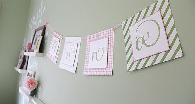 Pink and green paper garland on the nursery wall with letters that spell a baby girl's name