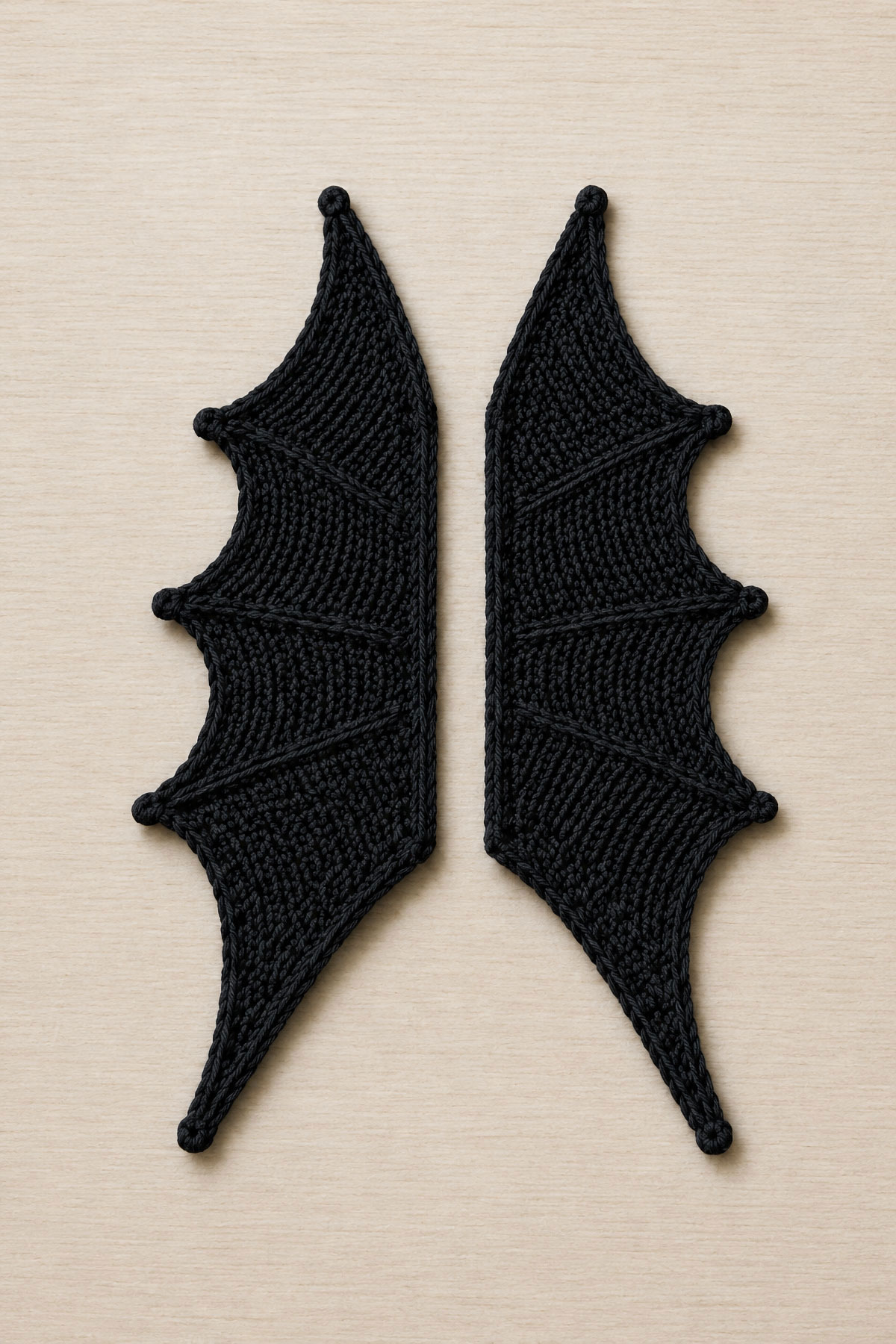 Two matching crochet bat wings positioned with straight attachment edges together and outer tips pointing in opposite directions