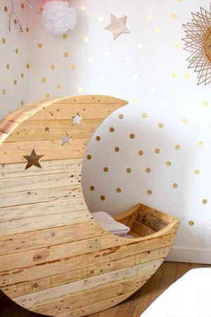 Crescent moon shaped handmade wooden baby cradle with a celestial stars theme for a shabby chic nursery room.