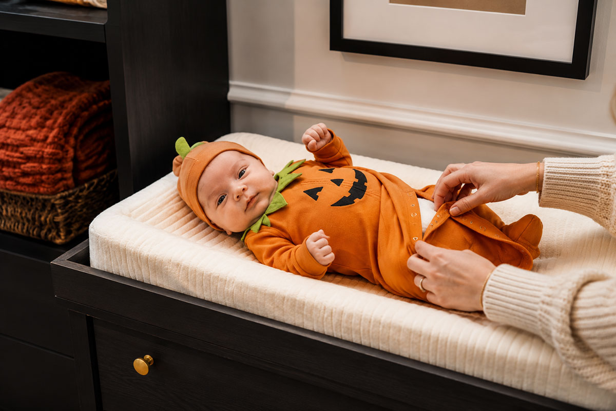 Newborn baby wearing a soft simple pumpkin Halloween outfit with easy diaper access