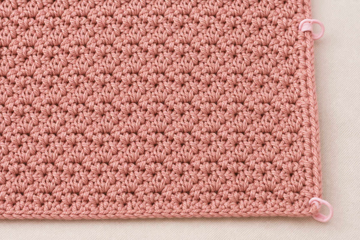 Close angled view of a straight crochet blanket edge with locking stitch markers identifying the first and last stitches