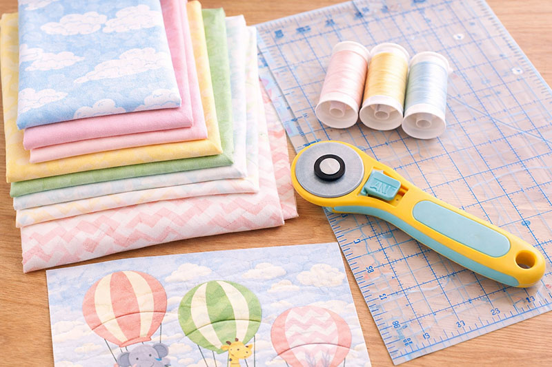 quilting supplies including rotary cutter ruler thread and fabric for crib quilt