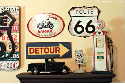 Gallery wall art display in a baby boy's Route 66 nursery theme including vintage road signs, an old, toy pickup truck and a miniature service station gas pump on a shelf