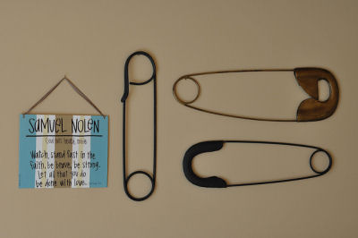 Large bronze baby diaper pins and a personalized verse used as decorations complete the nursery wall decor arrangement
