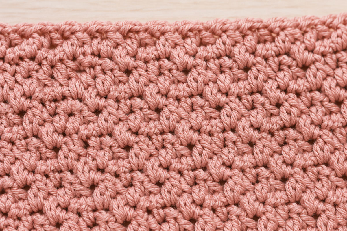 Close view of a single crochet, half double crochet and double crochet worked together to form a small slanted shell-style group