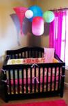 Colorful paper lanterns hung from the ceiling over the crib reflect the bright colors of the custom baby bedding.  